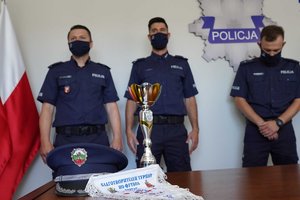 Policjanci z drużyny oczekujący na spotkanie z komendantem. Na stole przed nimi puchar, czapka i proporczyk