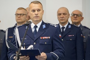 insp. Arkadiusz Sylwestrzak mówiący do mikrofonu i policjanci w tle