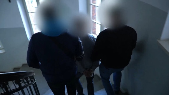 dwóch policjantów prowadzi osobę zatrzymaną