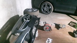 Fotografia kolorowa. Przedstawia wnętrze garażu, a w nim częściowo widoczny odzyskany samochód. Na posadzce narzędzia oraz części pochodzące z innego samochodu.