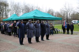 Fotografia kolorowa. Na zdjęciu policjanci oraz zebrani goście składający kwiaty przed grobem.