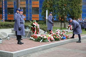 Fotografia kolorowa. Na zdjęciu policjanci oraz zebrani goście składający kwiaty przed grobem.