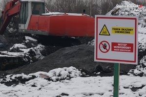 Zdjęcie przedstawia znak o treści &quot;TEREN SKAŻONY CHEMICZNIE. WSTĘP WZBRONIONY OBSZAR NIEBEZPIECZNY&quot;, w tle koparka