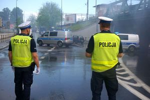 na zdjęciu umundurowani policjanci drogówki, którzy wstrzymują ruch samochodów, by umożliwić przejście kibicom