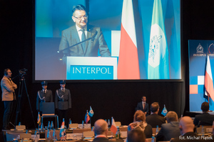 Zdjęcie przedstawia obraz z telebimu na którym wyświetlane jest przemówienie Wiceprezydenta Interpolu