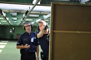 Instruktor strzelań policyjnych wraz z policjantem biorącym udział w turnieju par patrolowych, podczas konkurencji na strzelnicy. Policjant strzela zza przesłony