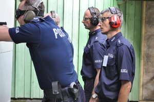 Policjanci podczas konkurencji na strzelnicy strzelają w kierunku tarcz, obserwują ich sędziowie - policyjni instruktorzy strzelań