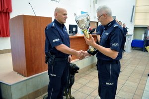 Zastępca Komendanta Wojewódzkiego Policji w Katowicach mł. insp. Mariusz Krzystyniak gratuluje zwycięzcy tegorocznego wojewódzkiego finału XIX Kynologicznych Mistrzostw Policji w garnizonie śląskim asp. sztab. Filipowi Waśniewskiemu z Komendy Miejskiej Policji  w Rybniku z psem Ibajon, do wyszukiwania zapachów materiałów wybuchowych.