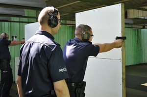 Instruktor policyjnych strzelań nadzoruje przebieg konkurencji ze strzelania. Strzelają dwaj policjanci
