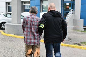 Policjant prowadzi zatrzymanego mężczyznę do budynku komendy