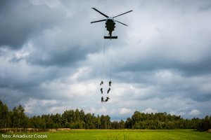 Zdjęcie kolorowe. Śmigłowiec w powietrzu, na jego pokładzie widoczni uczestnicy szkolenia