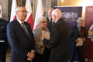 Zdjęcie kolorowe. Zdjęcie przedstawia wręczenie wyróżnienia za działalność społeczną uczestnikowi konferencji. Wyróżnienie wręcza poseł na Sejm RP Maria Nowak, Stanisław Szwed - Sekretarz Stanu w Ministerstwie Rodziny, Pracy i Polityki Społecznej, oraz wicewojewoda śląski Jan Chrząszcz.