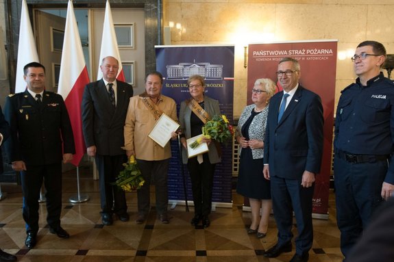 Zdjęcie kolorowe. Na zdjęciu widać od lewej nadbryg. Jacek Kleszczewski, Komendant Wojewódzki Państwowej Straży Pożarnej w Katowicach, wicewojewoda śląski Jan Chrząszcz, laureat konkursu Aktywny Senior Marek Wacław Judycki z Rudy Śląskiej, laureatka konkursu Aktywny Senior,  Renata Böhm ze Stowarzyszenia na rzecz odnowy i rozwoju lokalnego sołectwa Rudno,  poseł na Sejm RP Maria Nowak, Stanisław Szwed - Sekretarz Stanu w Ministerstwie Rodziny, Pracy i Polityki Społecznej, insp. Roman Rabsztyn, I Zastępca Komendanta Wojewódzkiego Policji w Katowicach.
