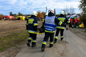 Strażacy przenoszą osobę poszkodowaną do Zespołu Ratownictwa Medycznego.