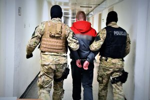 Na fotografii widać dwóch policjantów prowadzących zatrzymanego