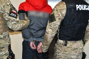 Na fotografii widać dwóch policjantów prowadzących zatrzymanego