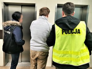 Policjanci wchodzą z zatrzymanym do windy.