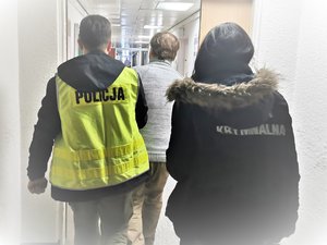 Policjanci prowadzą osobę zatrzymaną.