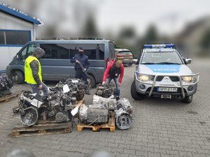 Zdjęcie kolorowe. Widoczni policjanci podczas zabezpieczania części samochodowych