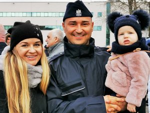 Policjant trzyma na ręku dziecko. Obok stoi młoda kobieta.