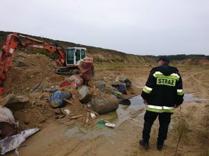 Zdjęcie kolorowe. Widoczne służby pracujące w miejscu ujawnienia nielegalnie składowanych odpadów