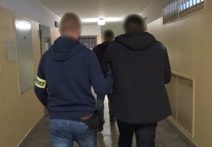 Zdjęcie kolorowe. Policjant doprowadza zatrzymanego na czynności procesowe