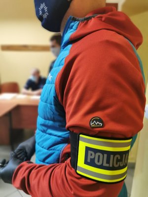 Zdjęcie kolorowe. Policjant z opaską z napisem o treści policja