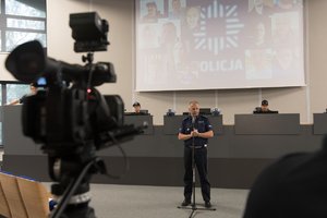 Zdjęcie kolorowe. Widoczny policjant podczas briefingu prasowego