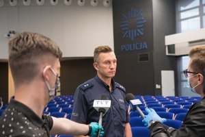 Zdjęcie kolorowe. Widoczny policjant podczas briefingu prasowego