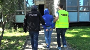 Policjanci prowadzą zatrzymaną kobietę.