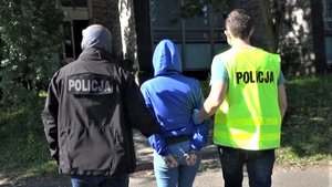 Policjanci prowadzą zatrzymaną kobietę.