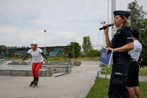 Policjantka przemawia do mirofonu, w tle zawodniczka na rolkach