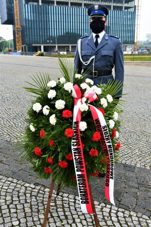 Policjant stoi z wieńcem kwiatów