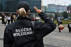 Funkcjonariuszka służby więziennej stojąca tyłem podczas oddawania honoru