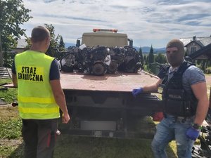 Zdjęcie kolorowe. Policjanci i funkcjonariusze straży granicznej zabezpieczają części samochodowe