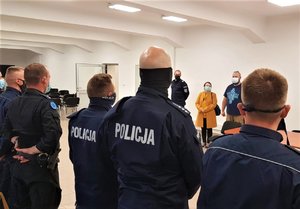 Umundurowani policjanci stoją w szeregu przed osobami, które prowadzą kurs.