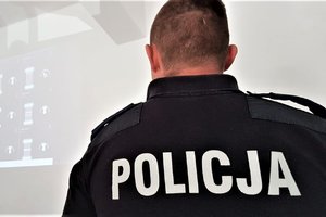 Umundurowany policjant siedzący przed ekranem, na którym wyświetlany jest pokaz.