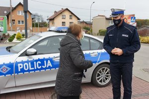 Umundurowany policjant rozmawia z kobietą, której wręczył odblaskową torbę. W tle policyjny radiowóz