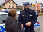 Umundurowany policjant rozmawia przy radiowozie z kobietą, której wręczył odblaskową torbę.