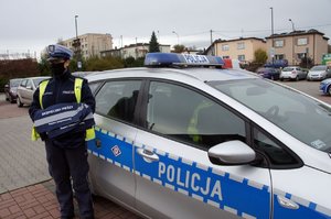 Umundurowana policjanta stoi przy radiowozie z odblaskowymi torbami dla seniorów.