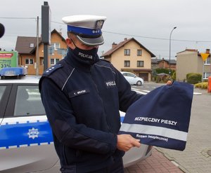 Umundurowany policjant trzyma w dłoniach odblaskową torbę, na której widnieje napis bezpieczny pieszy, razem bezpieczniej.