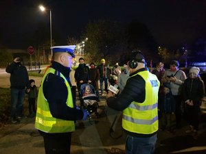 Policjant rozmawia z dziennikarzem, a w tle stoją osoby uczestniczące w akcji.