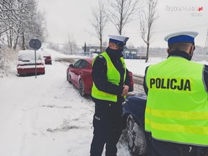 Policjanci w odblaskowych kamizelkach ewykonują czynności podczas kontroli drogowej.