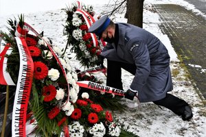 Umundurowany policjant składa wiązankę przed pomnikiem.