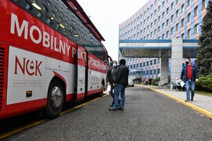 Na pierwszym planie znajduje się autobus, w którym oddawana jest krew. Widnieje na nim napis: mobilny punkt poboru krwi. Przed nim stoją osoby, w tle budynek katowickiej komendy wojewódzkiej.