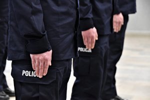 Dłonie stojących na baczność nowo przyjętych policjantów, zbliżenie na napis Policja na mundurze.