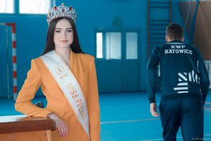 Zdjęcie kolorowe. Widoczna Miss Polski 2020 oraz plecy policjanta z bluza z napisem KWP Katowice na terenie hali sportowej. Autor zdjęcia: Michał Piątek