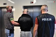 Kryminalni stoją z zatrzymanym mężczyzną przed windą, oczekując na jej przyjazd.