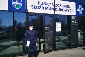 Policjantka stoi przy wejściu do punktu szczepień służb mundurowych.