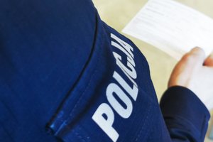 Policjant ogląda kartę szczepienia. Zbliżenie na jego rękaw z napisem policja.